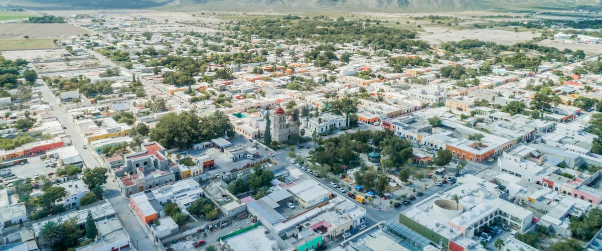 An aerial view of a town with a prominent church, surrounded by mountains and greenery.