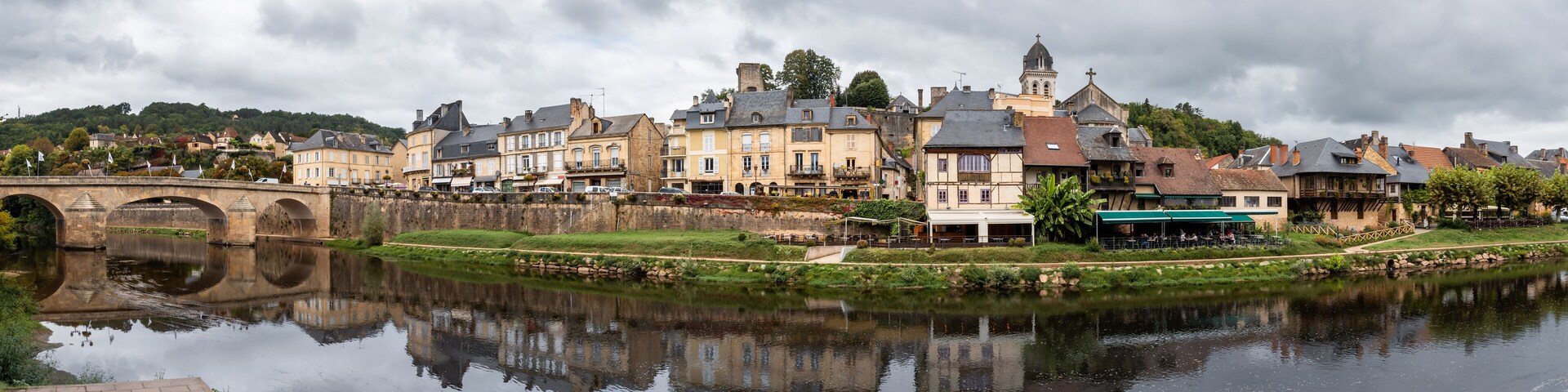 A river reflecting historic buildings, a stone bridge, and a church tower.