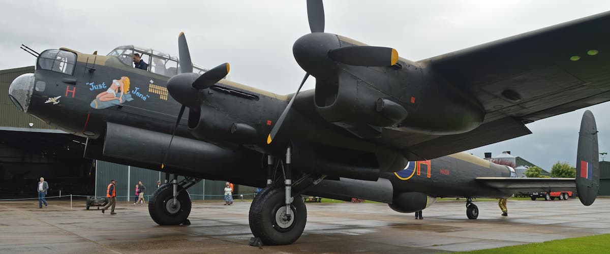 A vintage military aircraft with a propeller, painted in dark colors, parked on a tarmac with a grassy area in the foreground.