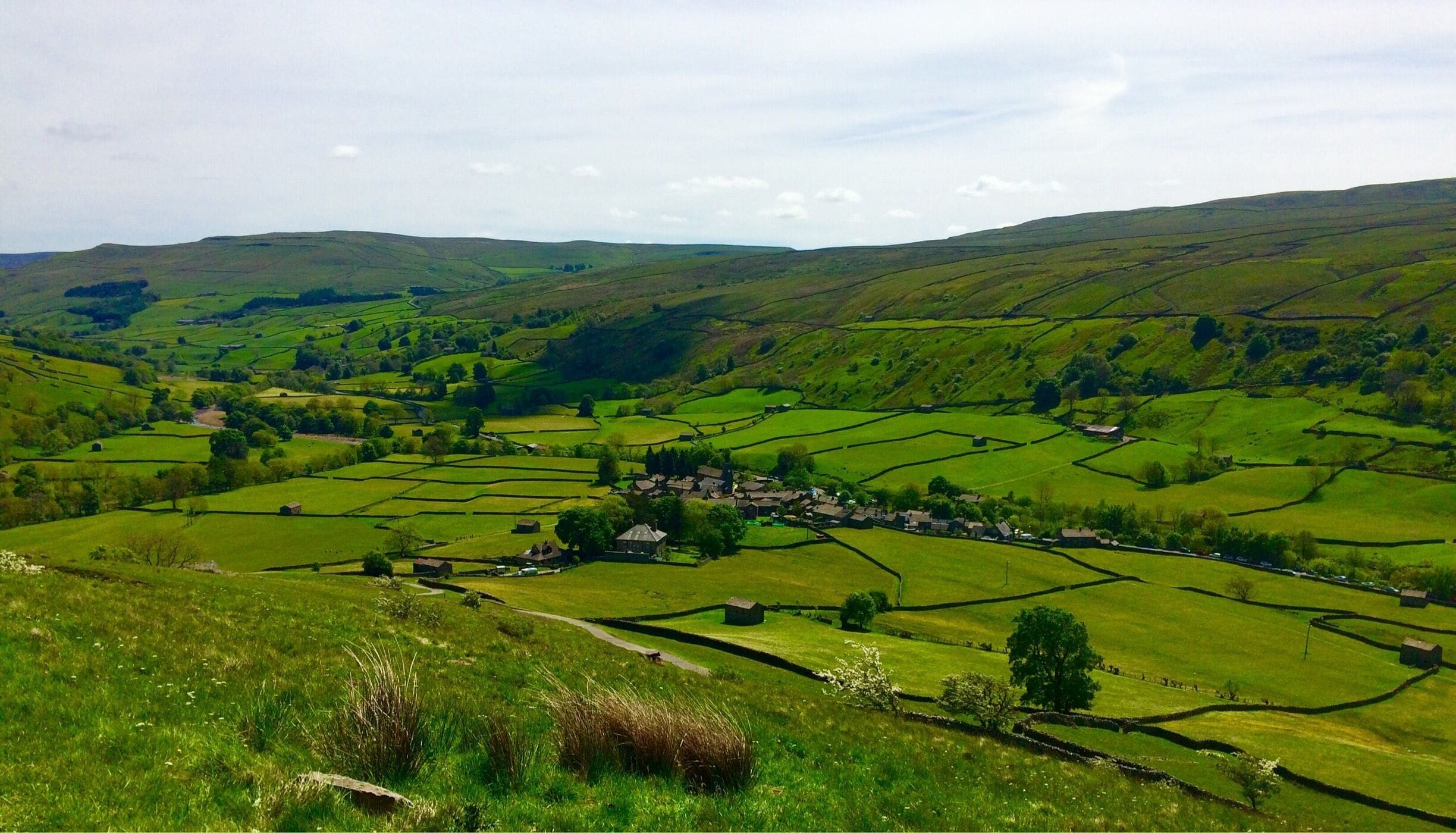 A rural landscape with rolling hills, green fields, and scattered stone walls.