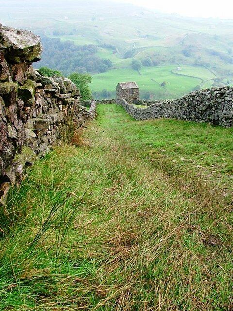 A stone wall and a small building in a grassy valley.