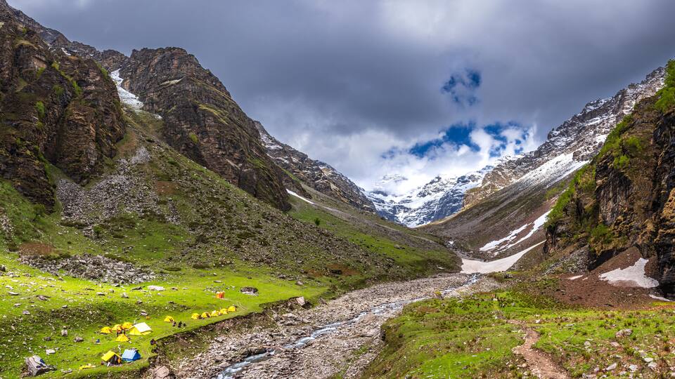 A mountainous landscape with a river, green grass, and tents.