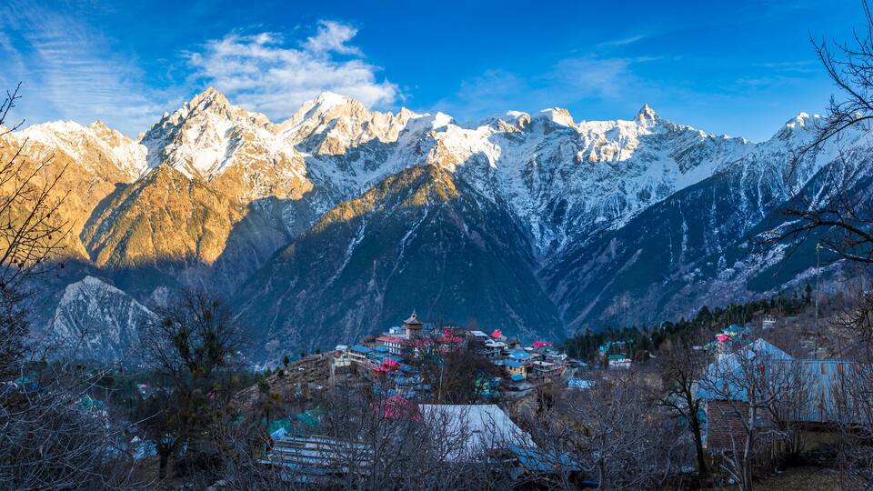 Snow-capped mountains, a village with colorful houses, and a clear blue sky.