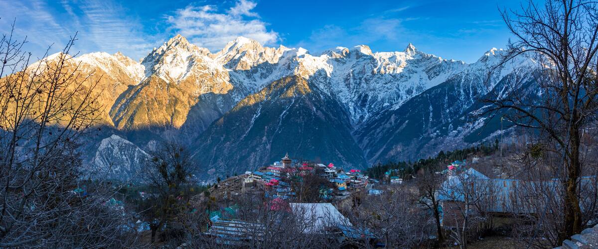 Snow-capped mountains, a village with colorful houses, and a clear blue sky.