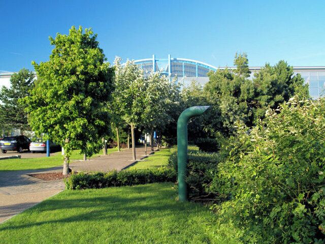 A green park with trees, a pathway, and a building with a blue roof in the background.