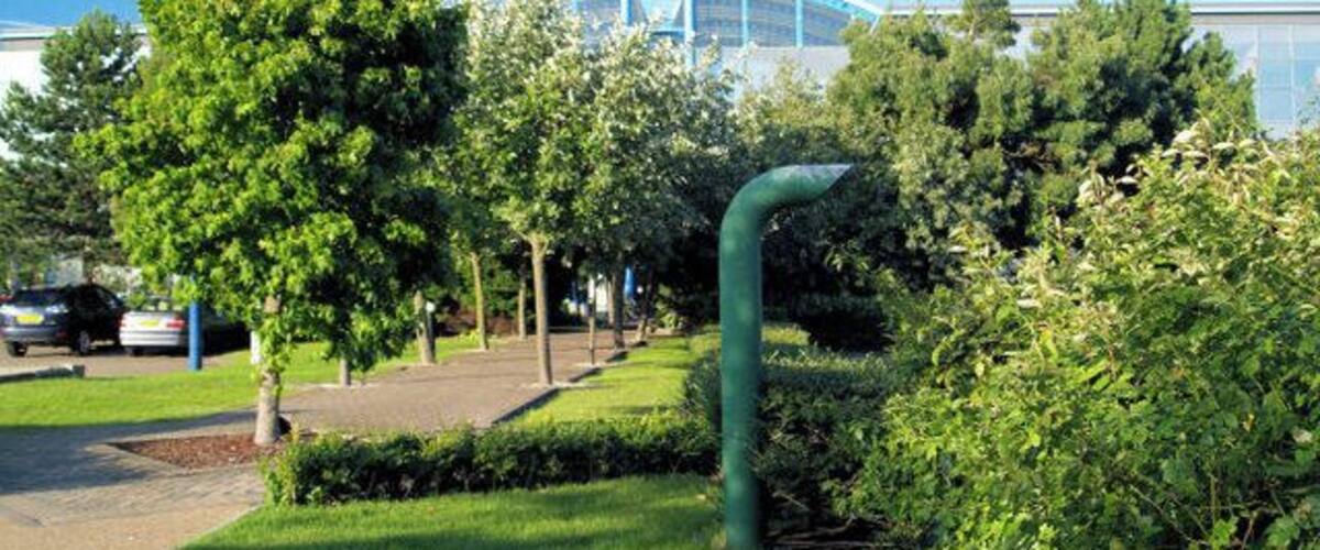 A green park with trees, a pathway, and a building with a blue roof in the background.