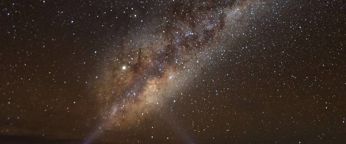A starry night sky with a visible Milky Way and two people standing on a flat landscape.