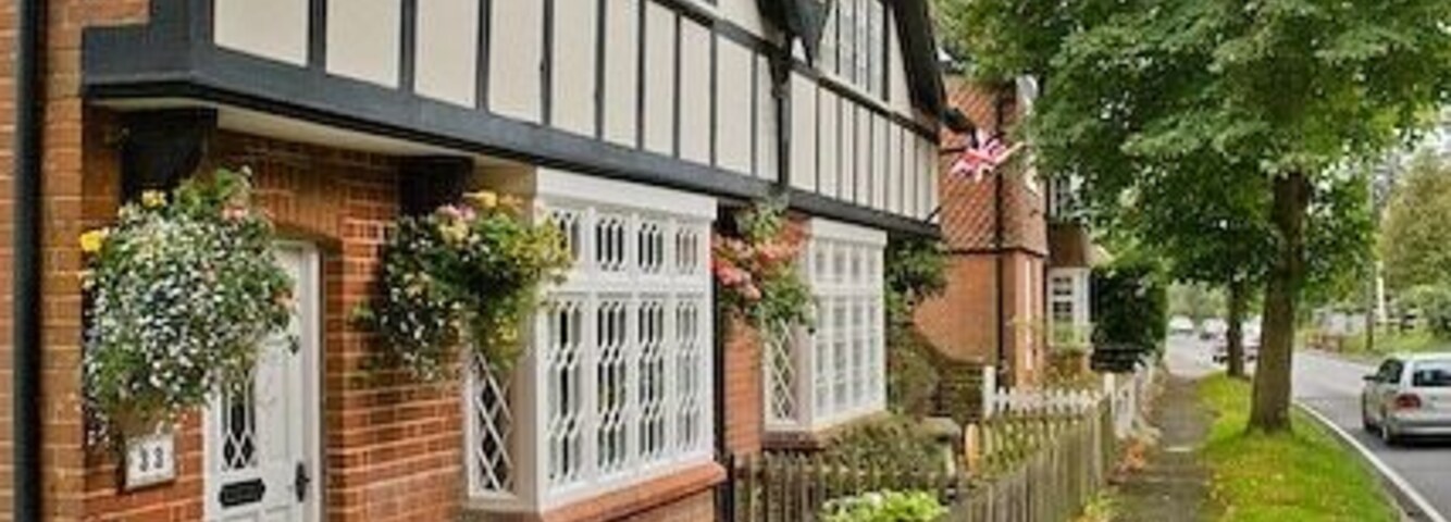 Fileira de casas em estilo Tudor com estrutura de madeira em preto e branco, cerca de madeira e um caminho pavimentado.
