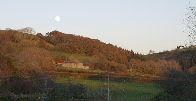 A rural landscape with a house on a hill, a field, and a body of water.