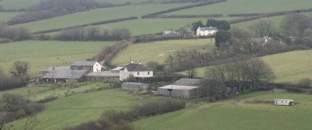 Rolling green fields, a white house, and several barns in a rural setting.