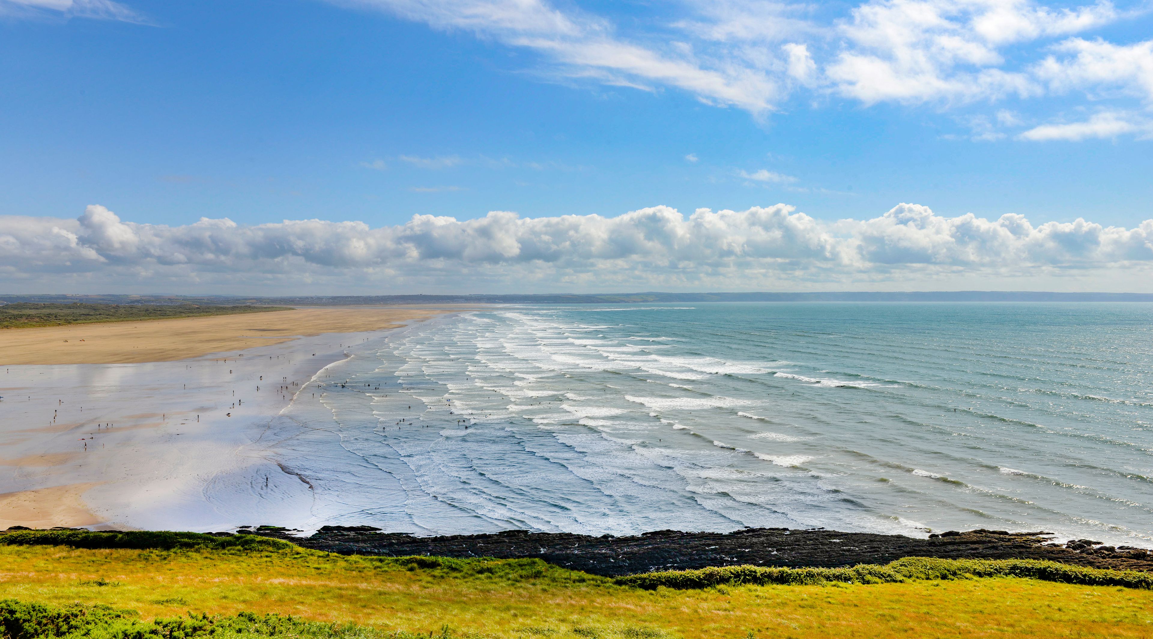 A coastal landscape with a sandy beach, ocean waves, and a grassy foreground.