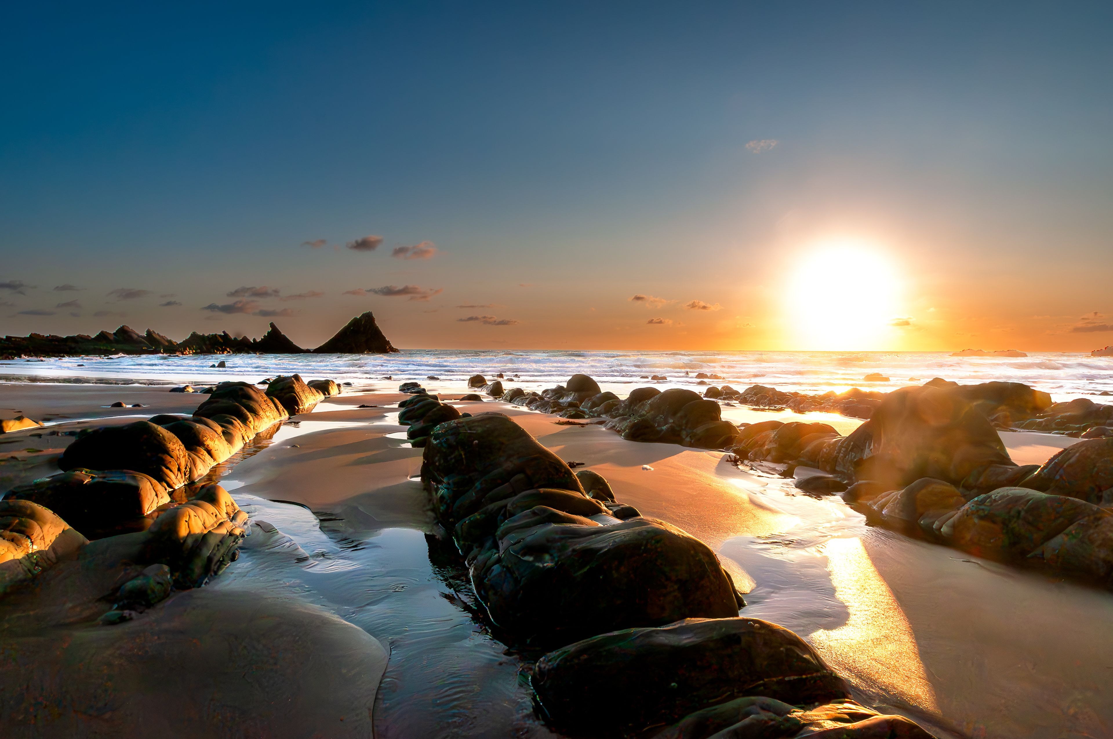 Una playa con grandes rocas y olas al atardecer.