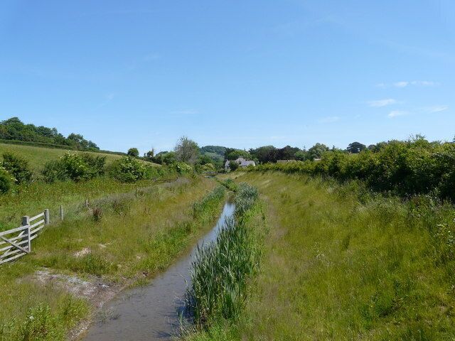A narrow water channel flanked by lush greenery and a wooden fence.