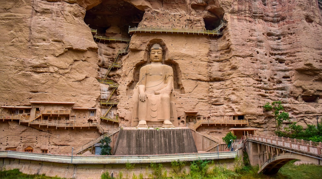 Una gran estatua de Buda tallada en la ladera de un acantilado, con un puente y senderos que conducen a ella.