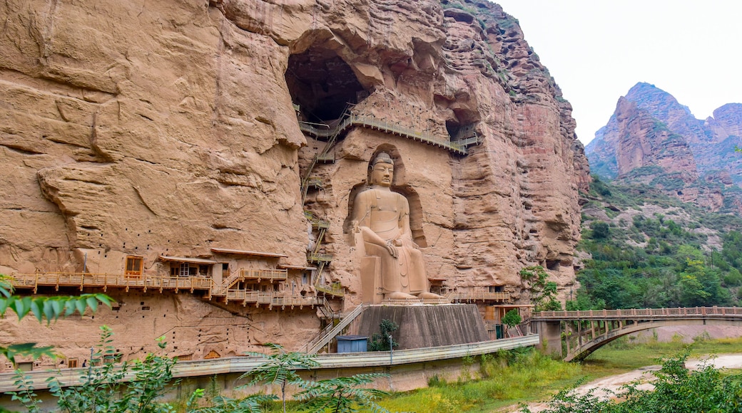 Una gran estatua de Buda tallada en un acantilado, con un puente y edificios circundantes.