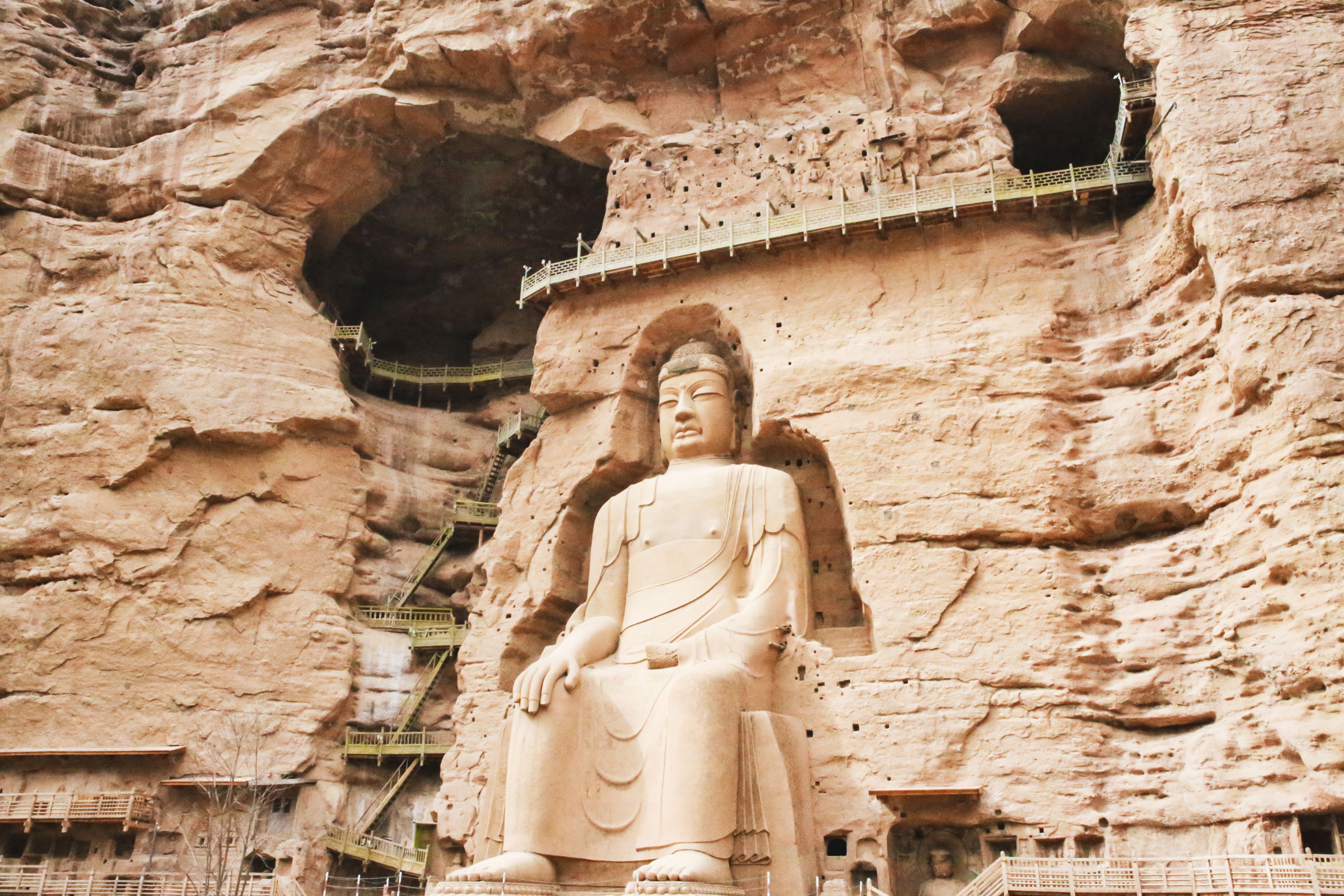 Una gran estatua de Buda tallada en un acantilado, con una plataforma de observación y escaleras que conducen hacia ella.