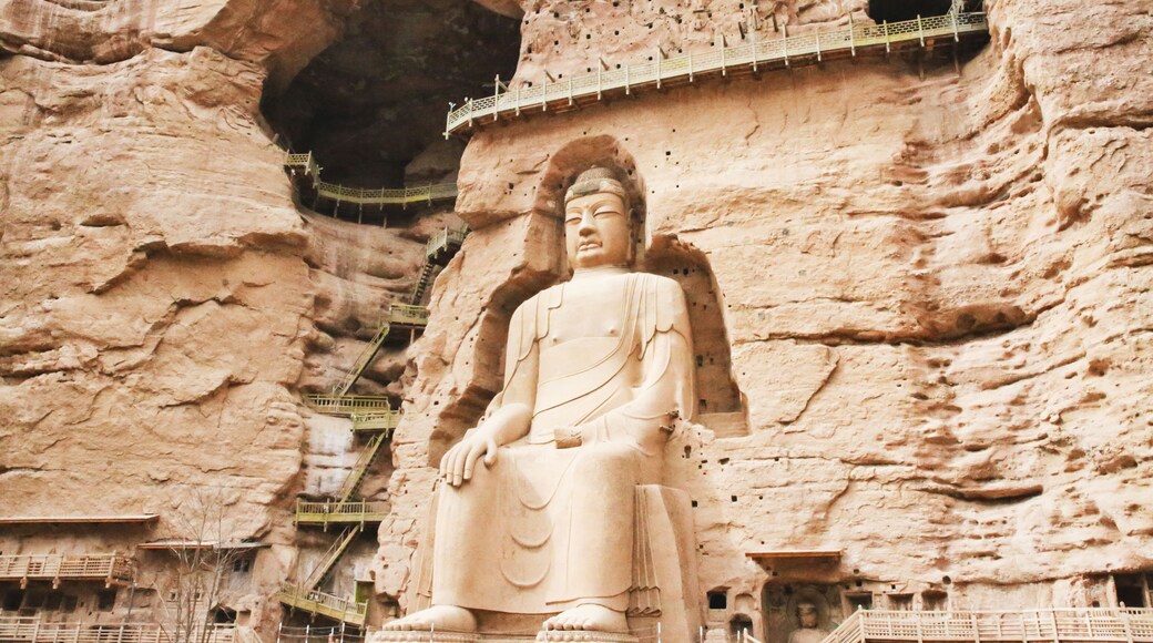 Una gran estatua de Buda tallada en un acantilado, con una plataforma de observación y escaleras que conducen hacia ella.
