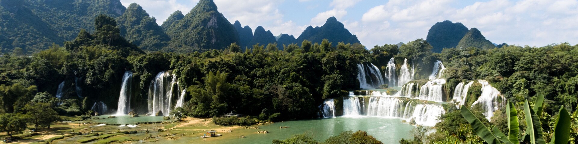 A series of waterfalls cascading into a river surrounded by lush greenery and mountains.