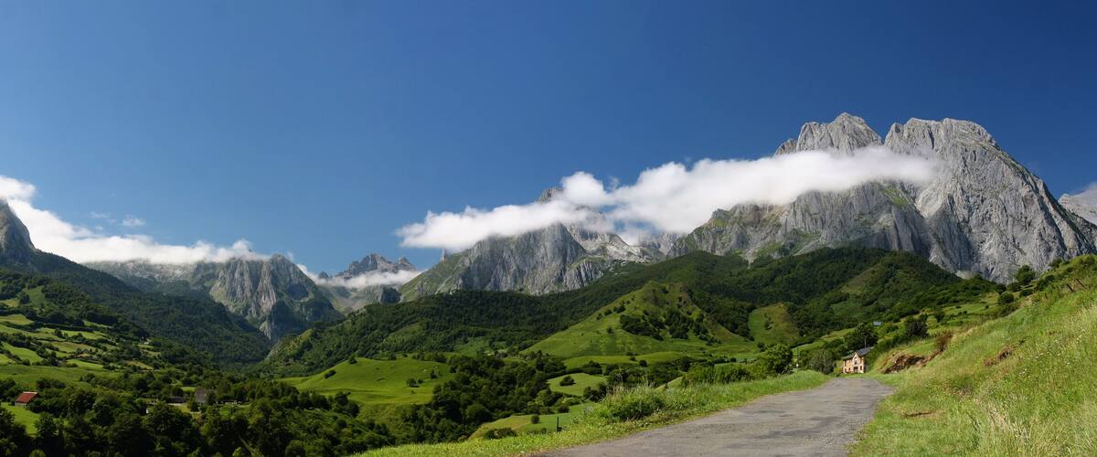 A mountainous landscape with a clear sky, a winding road, and a small house on the right.