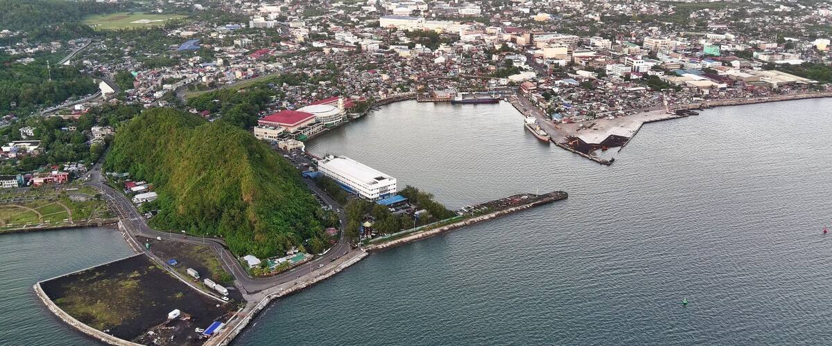 An aerial view of a coastal town with a prominent hill, a harbor, and a mix of residential and commercial buildings.