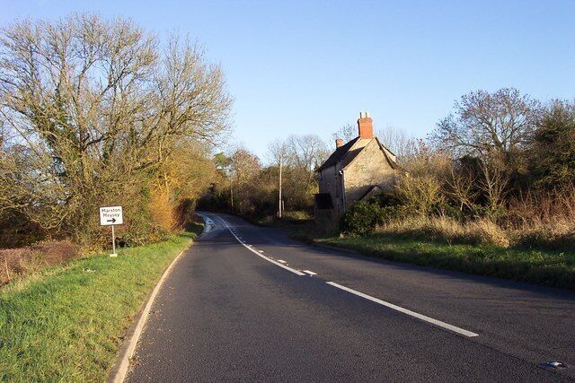 A rural road with a stone house on the right and a directional sign on the left.