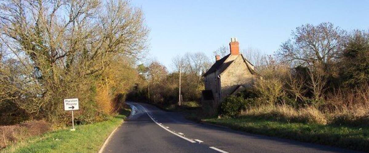 A rural road with a stone house on the right and a directional sign on the left.