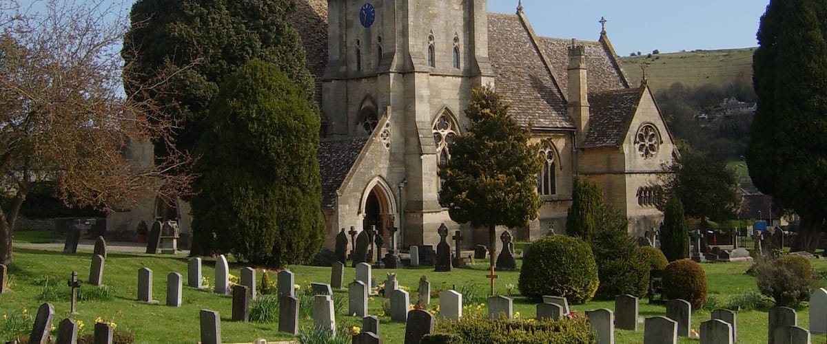 A church with a tall spire and a cemetery in the foreground.