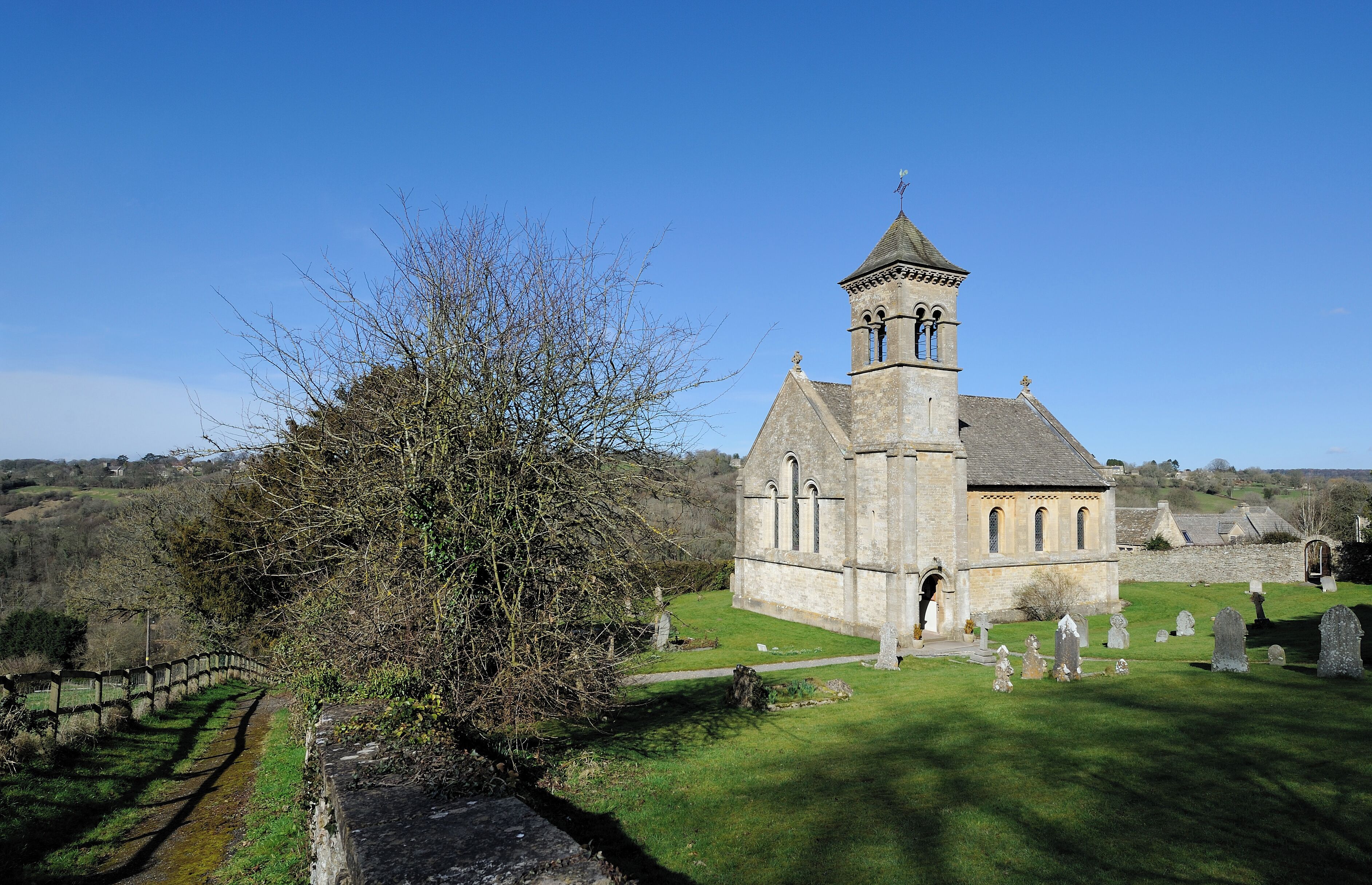 A church with a bell tower, surrounded by a cemetery and a stone wall.