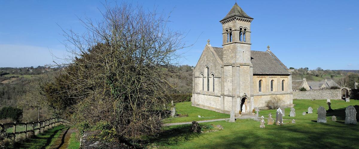 A church with a bell tower, surrounded by a cemetery and a stone wall.