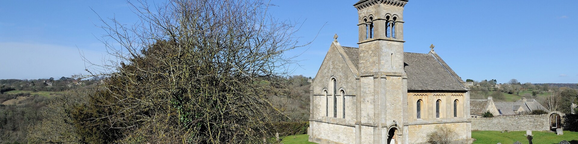 A church with a bell tower, surrounded by a cemetery and a stone wall.