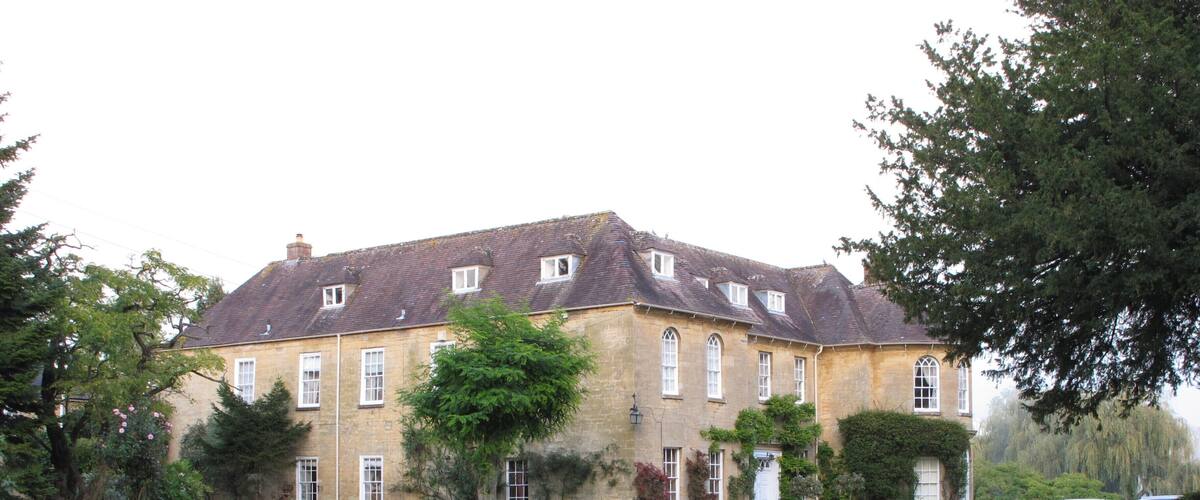 A large, historic stone building with a symmetrical facade, surrounded by a well-manicured lawn and mature trees.