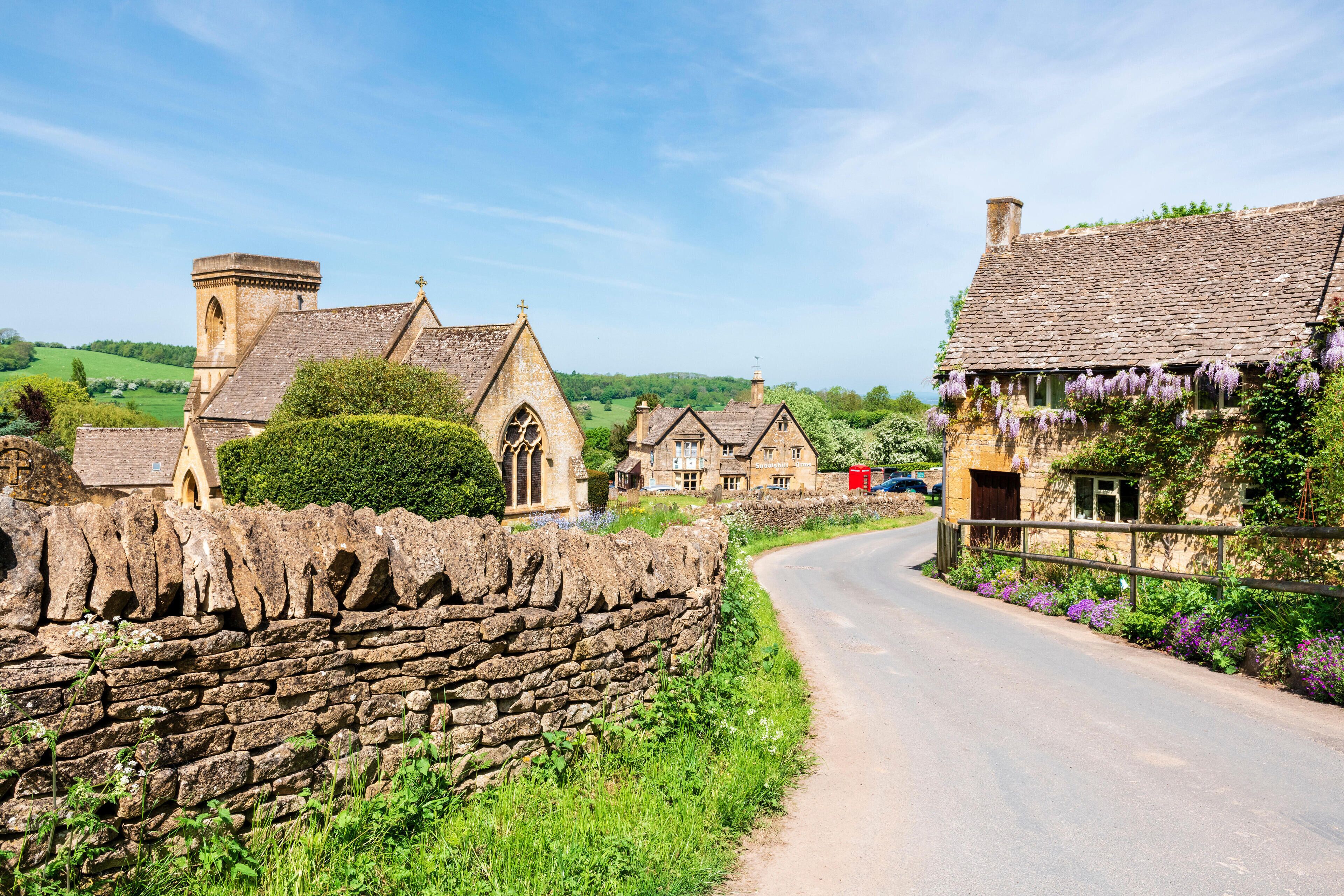 A stone wall, a church, and houses with purple flowers along a country road.