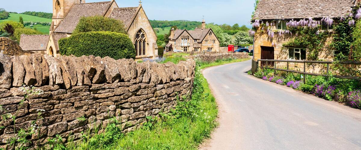 A stone wall, a church, and houses with purple flowers along a country road.