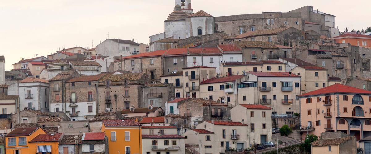A densely packed hillside town with historic buildings, a prominent church with a bell tower, and a steep street descending from the hill.