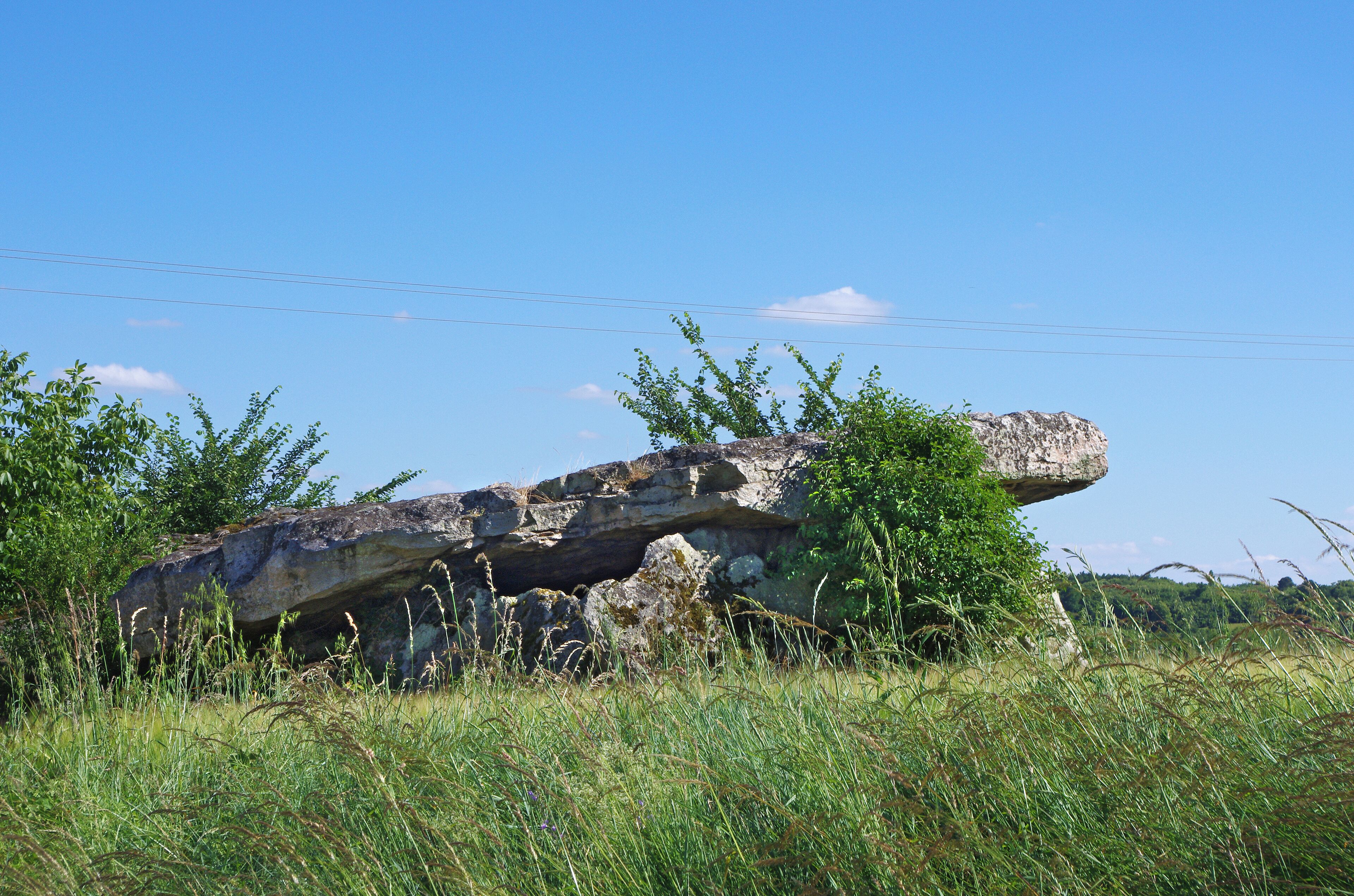A large rock formation in a grassy field with a clear blue sky.