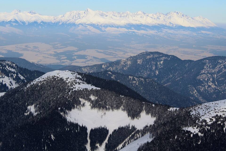 A snow-covered mountain range with dense forests and a distant snow-capped peak.