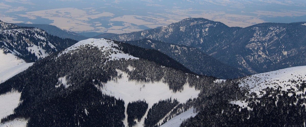 A snow-covered mountain range with dense forests and a distant snow-capped peak.