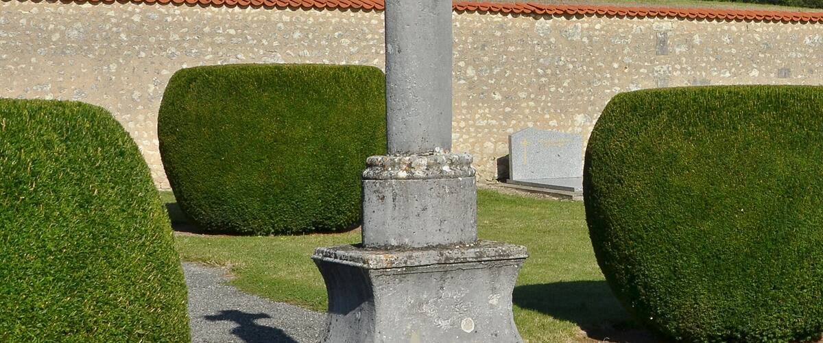 A stone cross in a cemetery with neatly trimmed hedges and a clear blue sky.