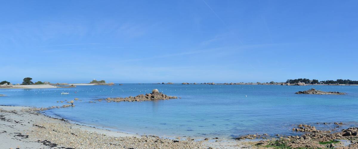 A coastal landscape with clear blue waters, rocky outcrops, and a sandy beach.