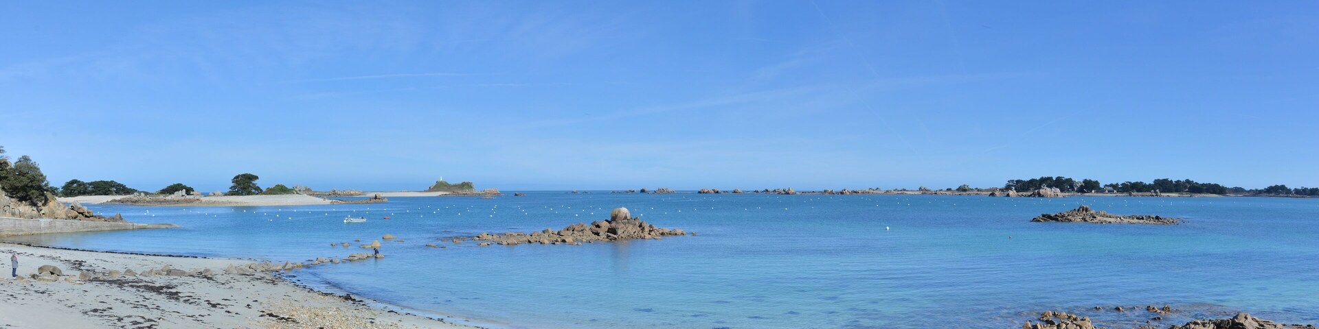 A coastal landscape with clear blue waters, rocky outcrops, and a sandy beach.
