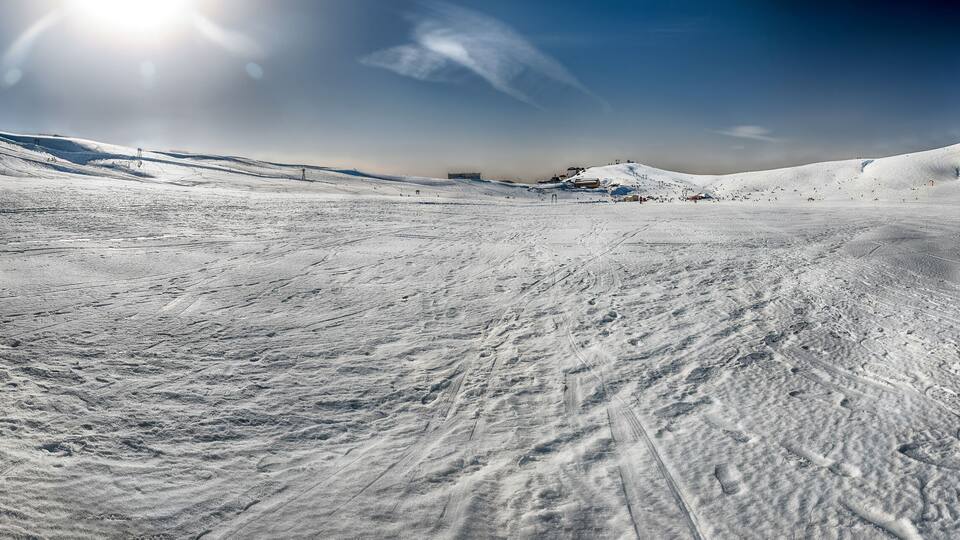 A snow-covered ski slope with ski tracks and a clear sky.