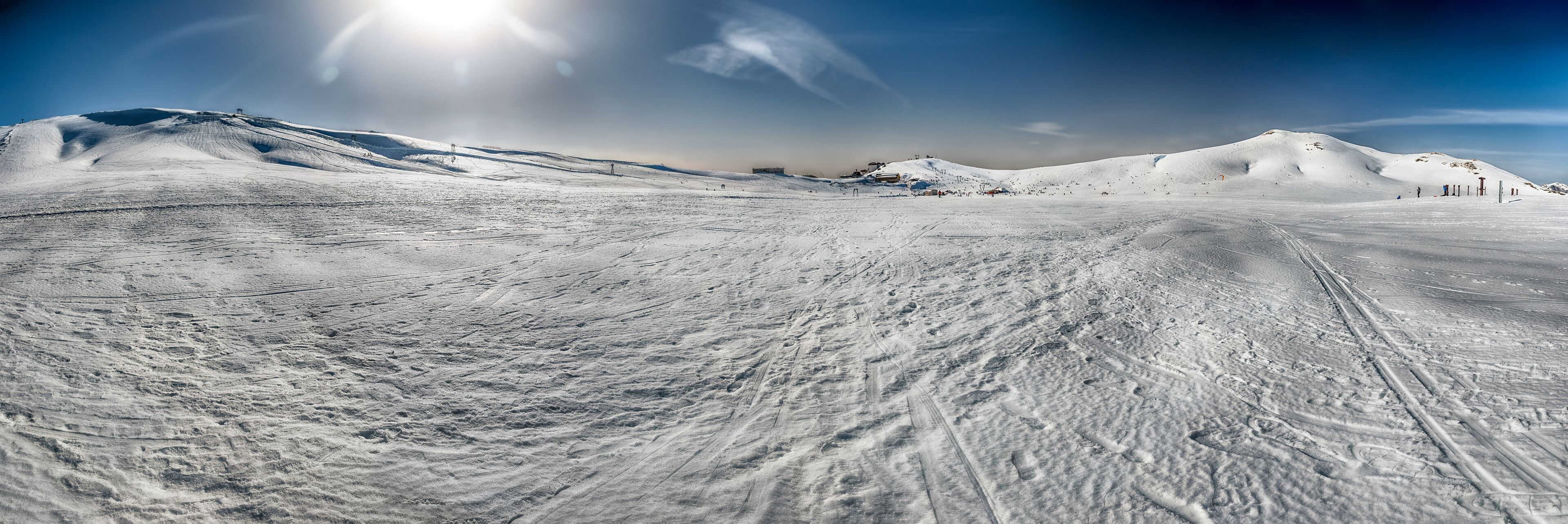A snow-covered ski slope with ski tracks and a clear sky.