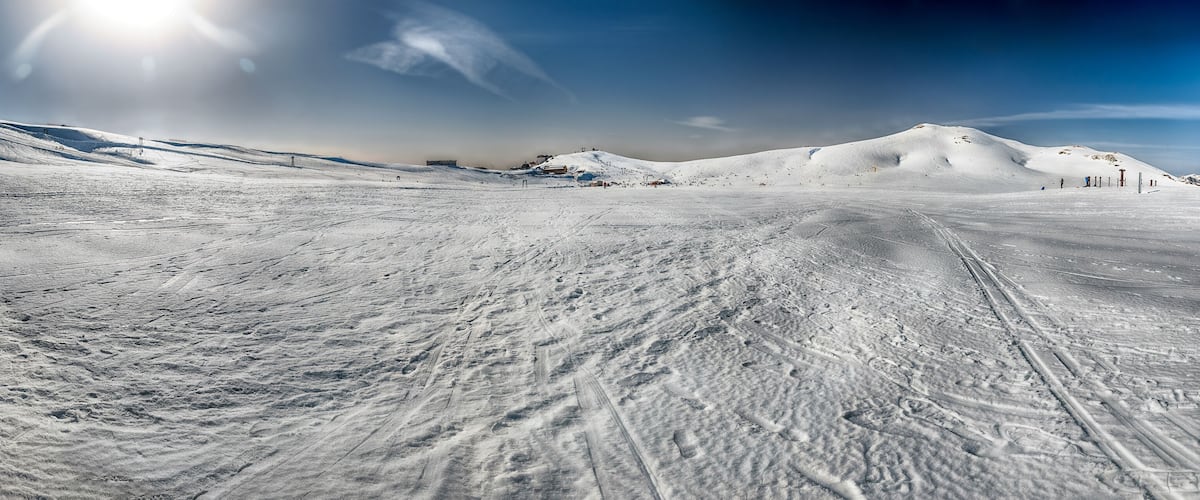 A snow-covered ski slope with ski tracks and a clear sky.