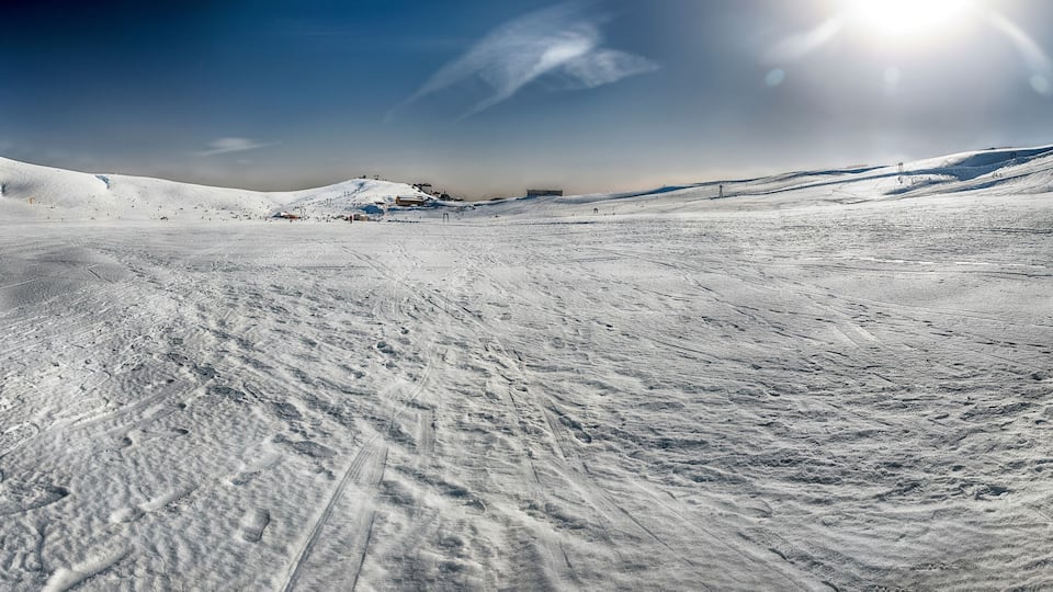 A snow-covered ski slope with ski tracks and a clear blue sky.