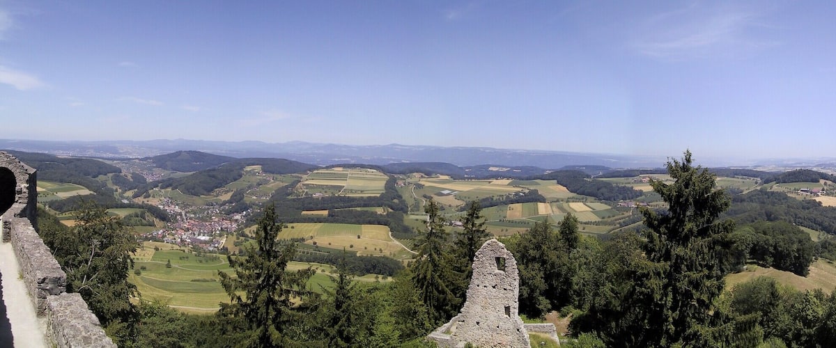 A panoramic view of a valley with rolling hills, a stone structure in the foreground, and a distant town.