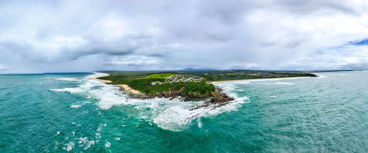 A coastal landscape with a small island, a beach, and a mountainous background.