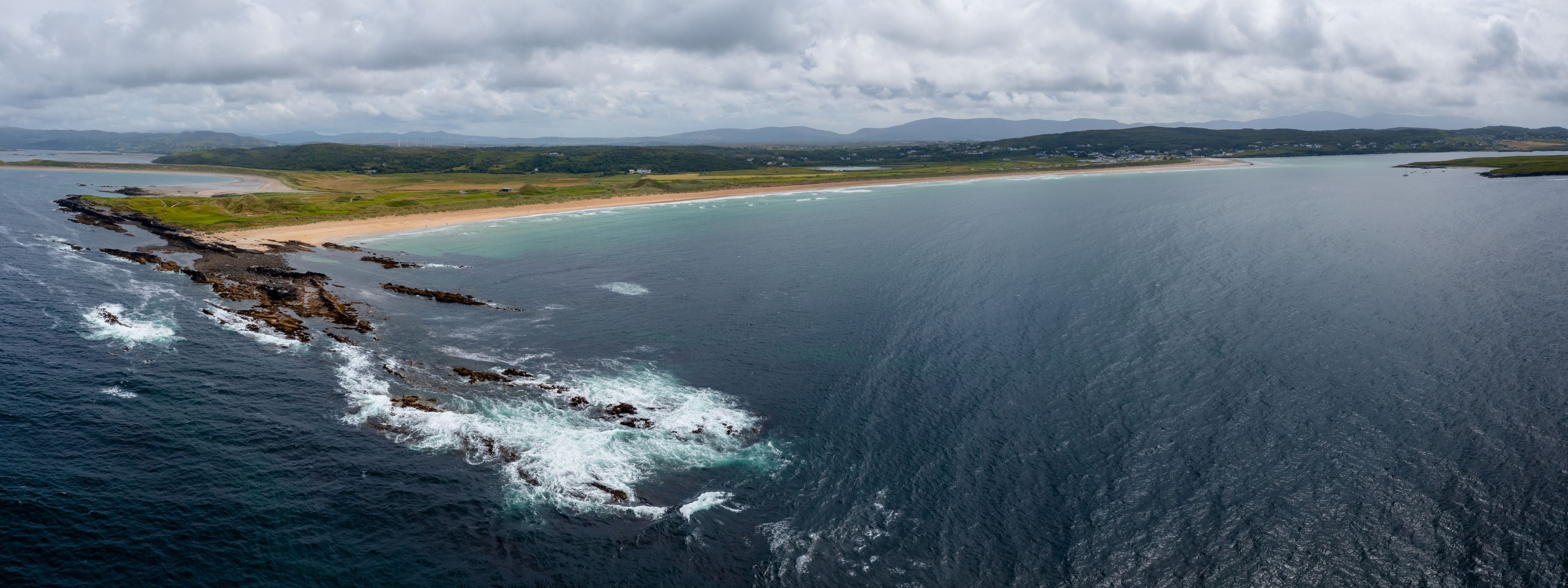 A coastal landscape with a rocky shoreline, a sandy beach, and a calm sea.