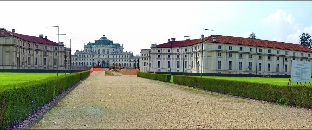 A grand building with a central dome and symmetrical wings, surrounded by a well-manicured lawn and gravel path.
