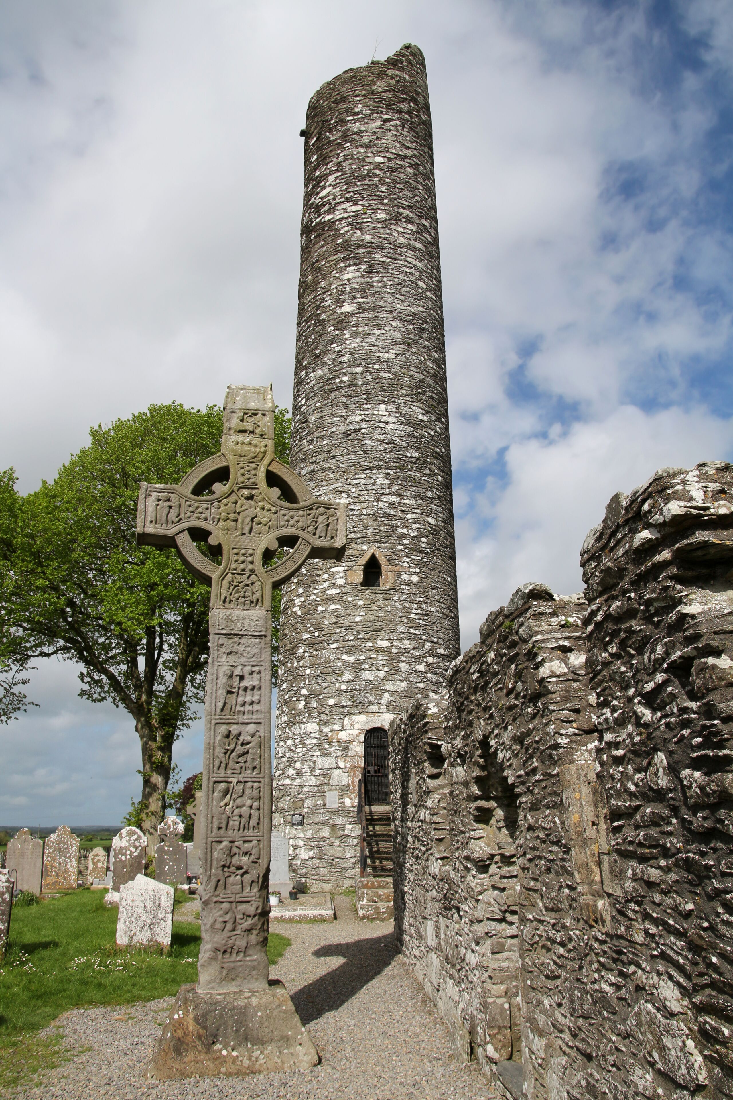 A stone cross and a cylindrical tower in a cemetery.