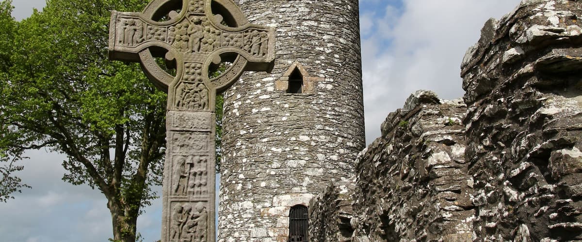 A stone cross and a cylindrical tower in a cemetery.